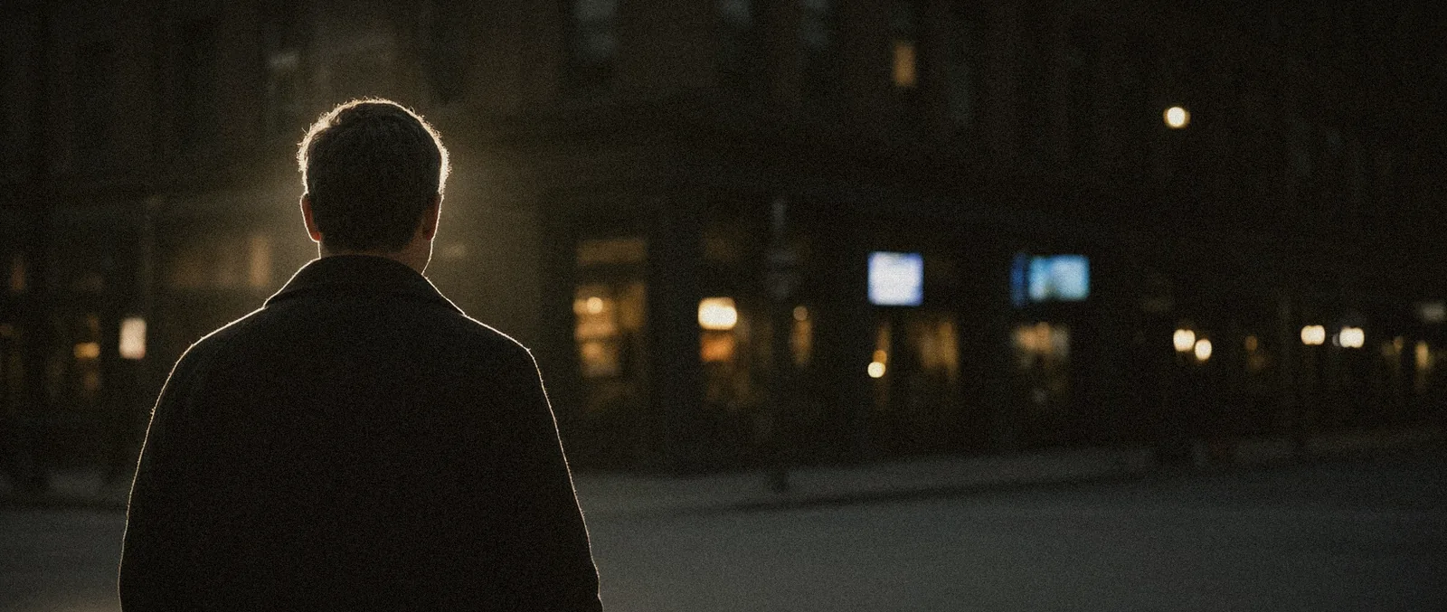 A business owner seen from behind, warm light around him on a city street at dusk